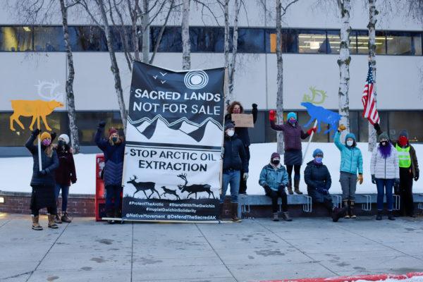 a group of people standing with a sign that reads "sacred lands not for sale; stop arctic oil extraction"